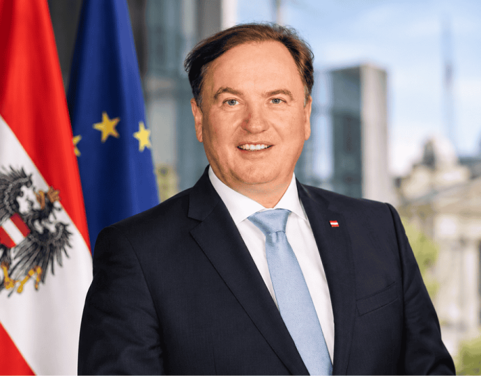 Portrait von Bernd Hinteregger vor den Flaggen Österreichs und der EU